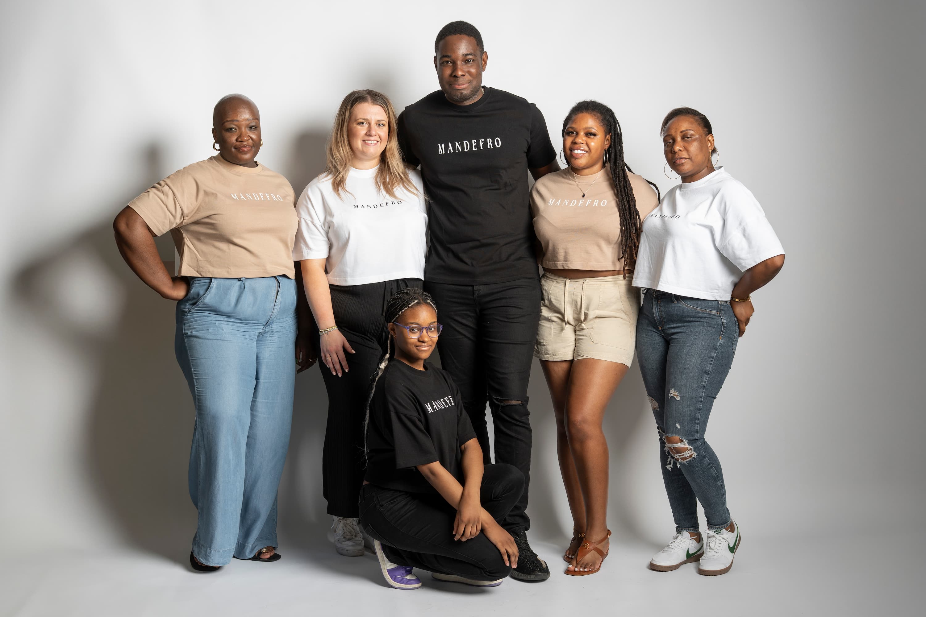 Group of six people posing together in Mandefro t-shirts against a plain backdrop