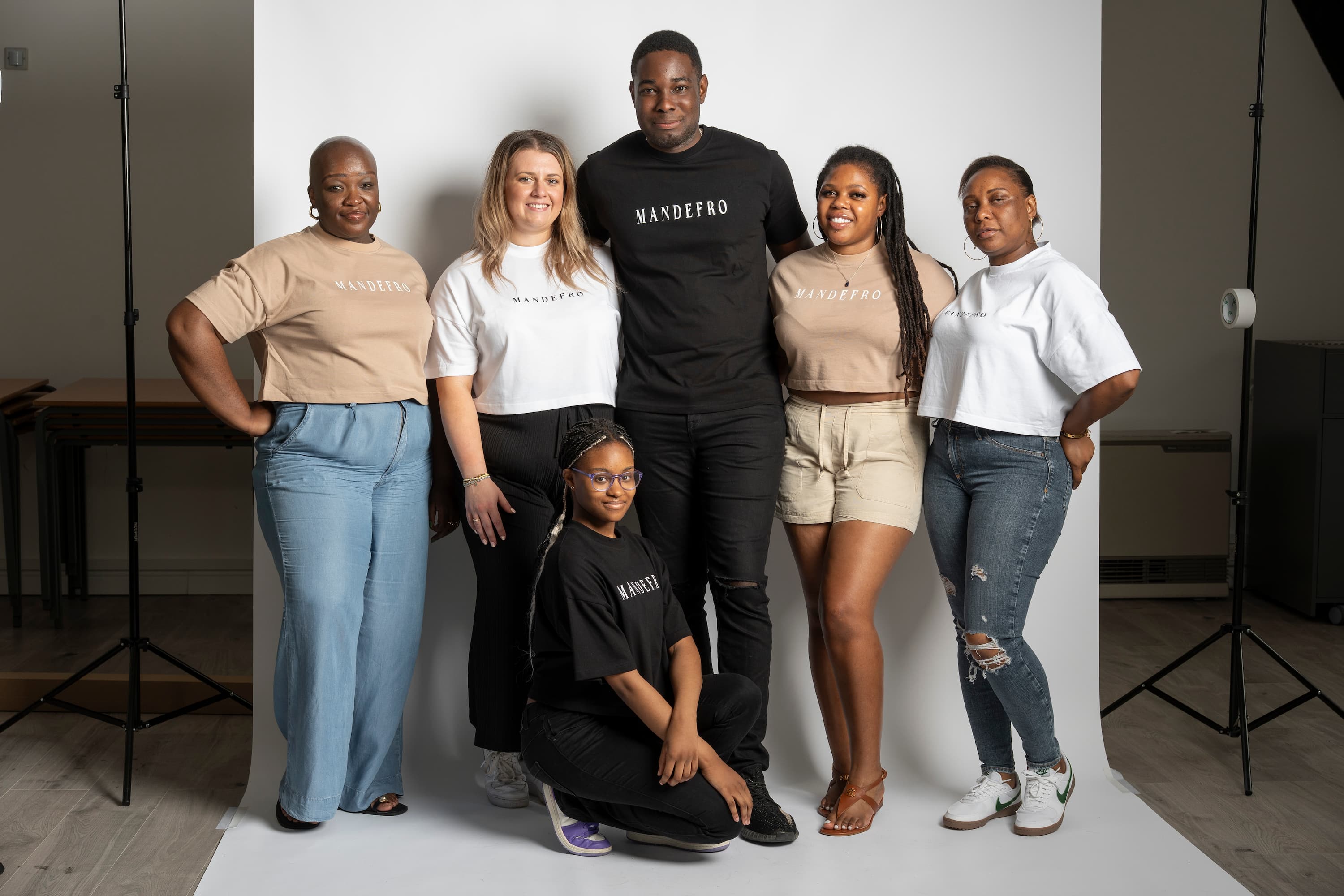 Group of six people posing in Mandefro tees in front of a white backdrop