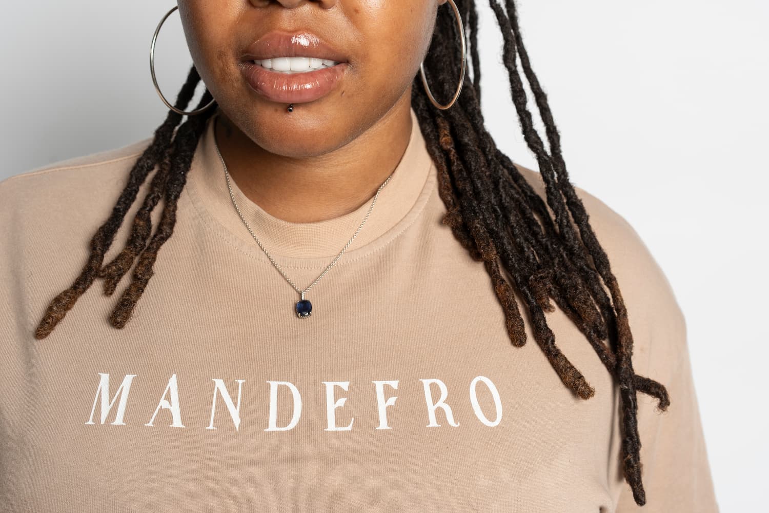 Woman wearing a beige sweatshirt with 'MANDEFRO' text on a plain background
