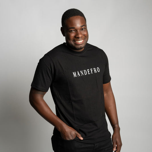 Man wearing a black t-shirt with 'MANDEFRO' text in front of a gray backdrop