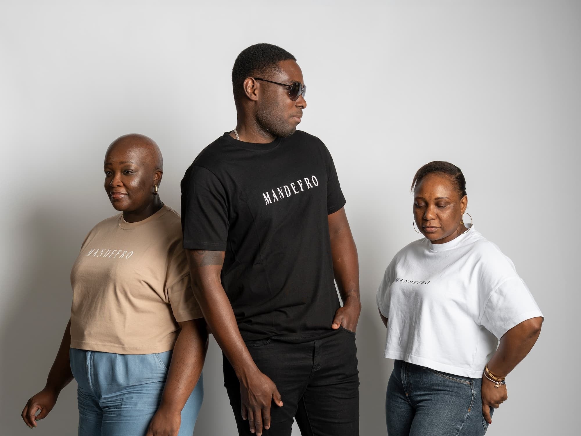 Three people standing side by side against a plain background, wearing branded t-shirts.