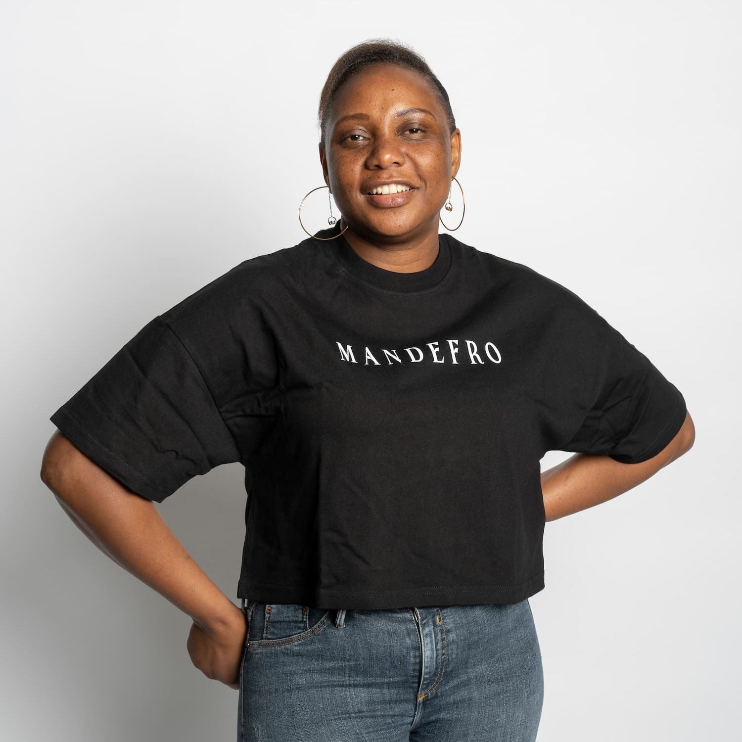Woman wearing a black cropped t-shirt with 'MANDEFRO' text on a plain background