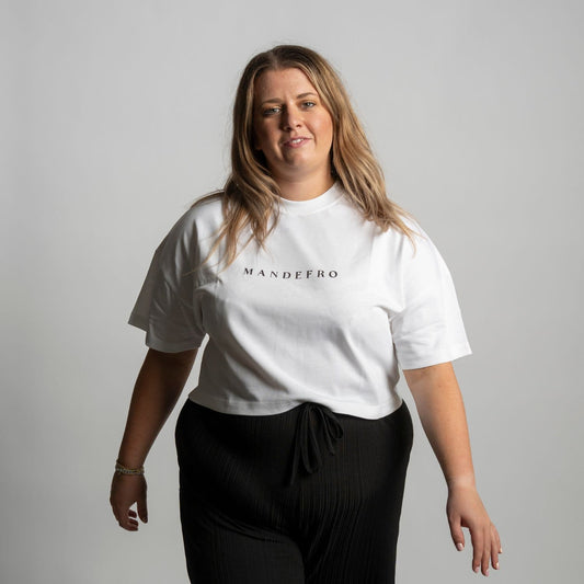 Woman wearing a white cropped t-shirt with 'MANDEFRO' logo on a plain background